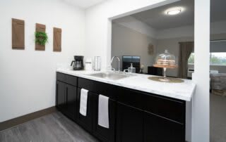 A modern kitchen with black cabinets and a marble countertop, featuring a coffee maker, sink, and a cake stand.