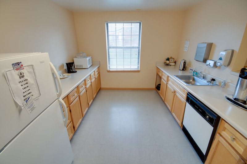 A tidy and compact kitchen with wooden cabinets, featuring appliances like a refrigerator, microwave, and dishwasher.