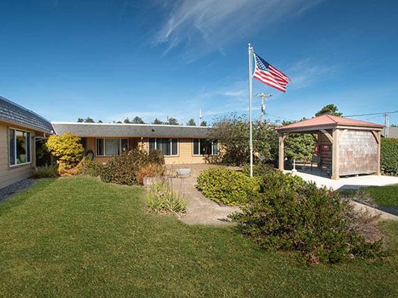 A suburban house with a neatly landscaped yard and a flagpole displaying the American flag under a clear blue sky.
