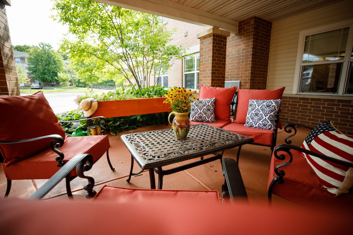 A cozy patio area with orange and patterned cushions, a decorative table, and potted flowers.