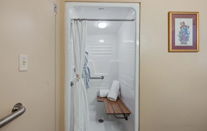 An accessible shower with a bench and grab bar, equipped with towels.