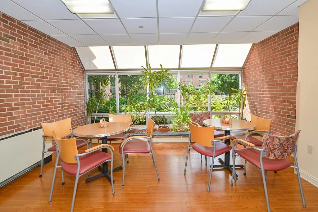 A well-lit indoor seating area with tables, chairs, and large windows overlooking greenery.