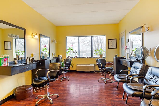 A bright and inviting hair salon interior with yellow walls, wooden flooring, and multiple styling stations.