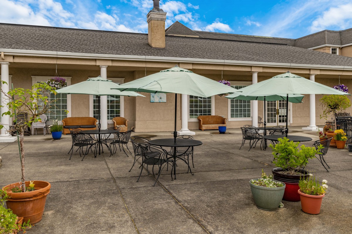 A well-furnished outdoor patio with tables, chairs, and umbrellas in front of a building.
