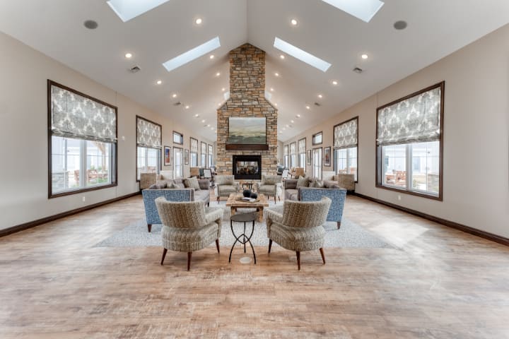 A spacious and modern living room featuring a central fireplace, multiple seating areas, wooden flooring, and natural light from skylights.