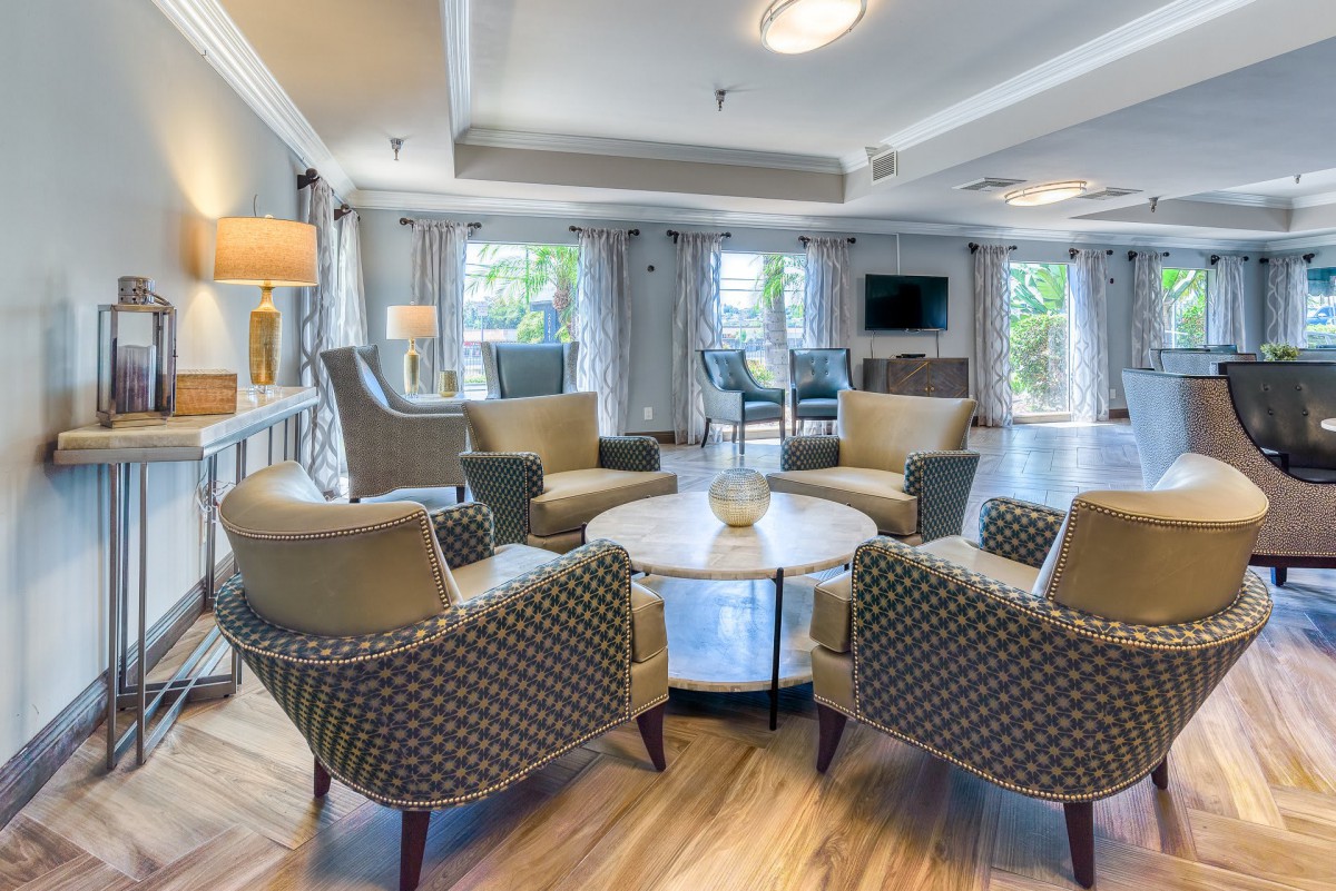 A modern living room with comfortable chairs arranged around a central table, featuring large windows and elegant decor.