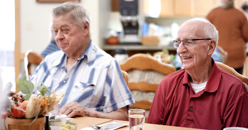 Two elderly men enjoying a meal together, sharing smiles and conversation.