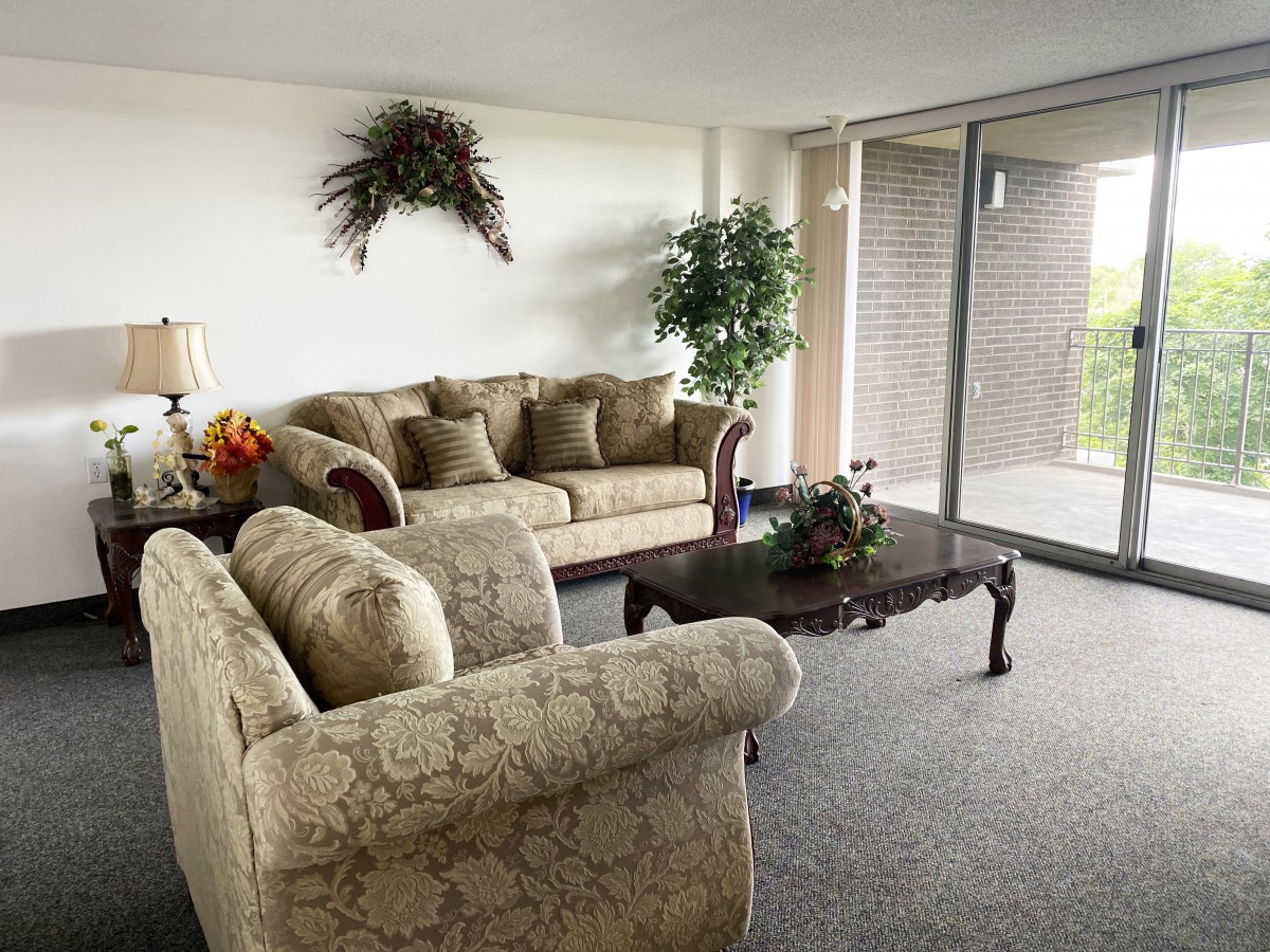 A cozy living room with elegant sofas and a coffee table, adorned with indoor plants and natural light streaming through large glass doors.