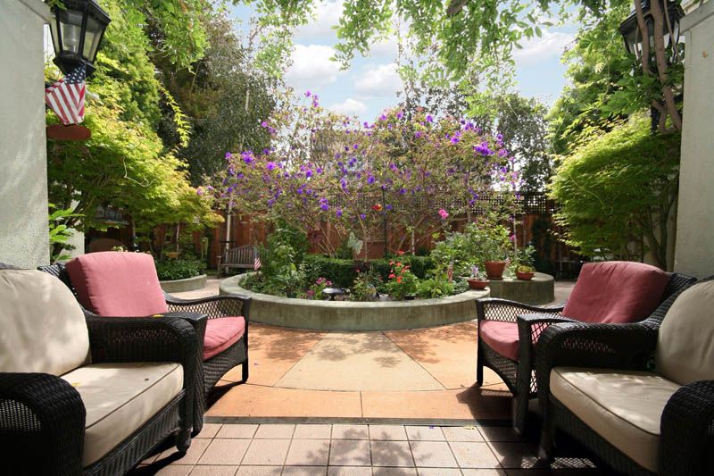A serene garden patio with comfortable seating and lush greenery surrounding a central fountain.