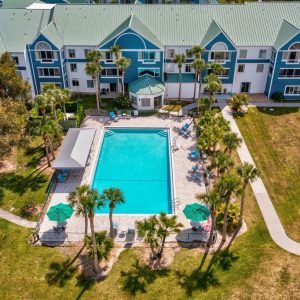 Aerial view of an apartment building with a central swimming pool surrounded by palm trees.