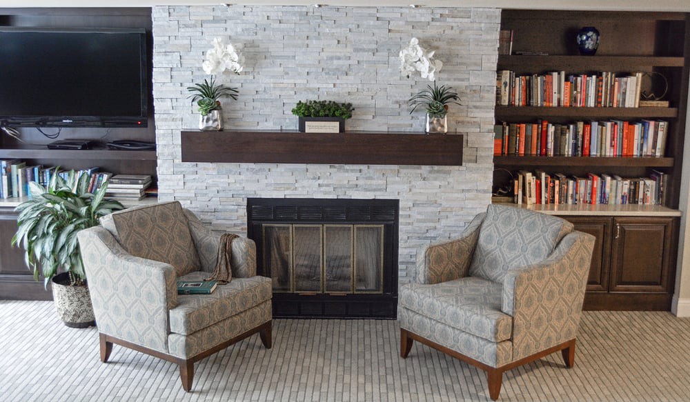 A cozy living room area with a fireplace, two armchairs, and decorative elements including books and indoor plants.