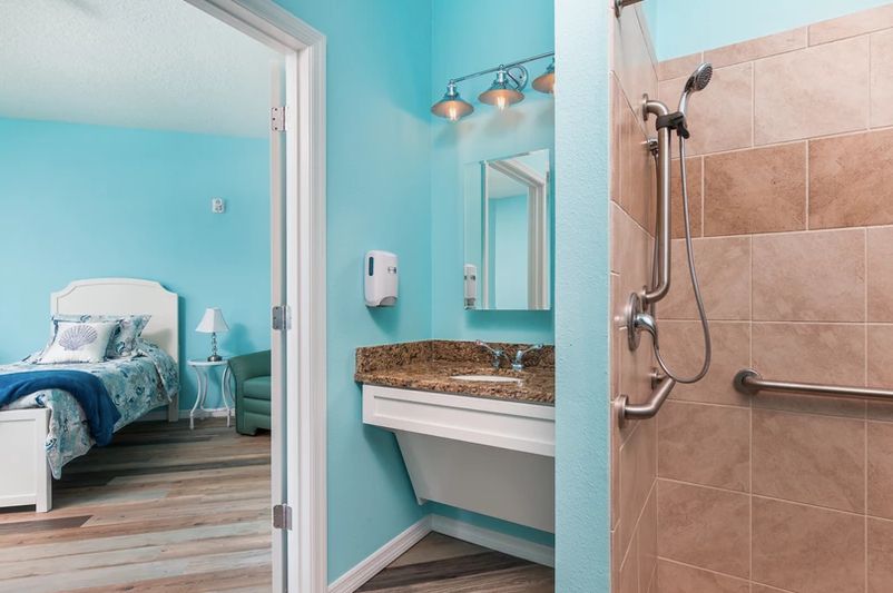 An accessible bathroom with turquoise walls, featuring a shower and wide sink area.