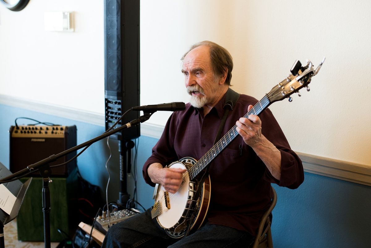 A man playing the banjo while singing into a microphone indoors.