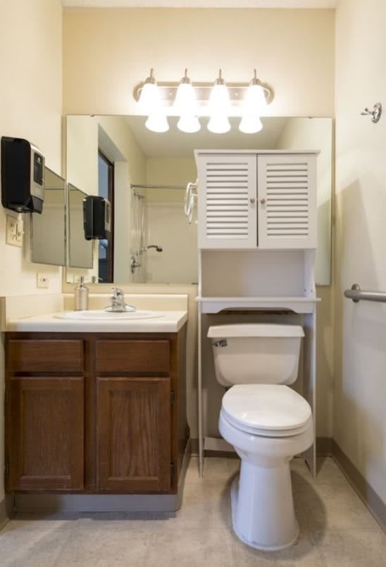 A small bathroom with a toilet, sink, mirror, and storage cabinet over the toilet.