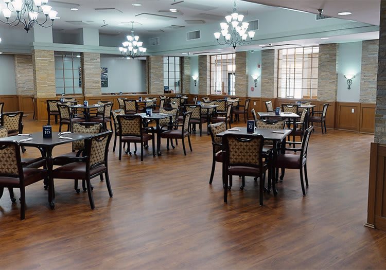 An empty dining area with neatly arranged tables and chairs under elegant chandeliers.