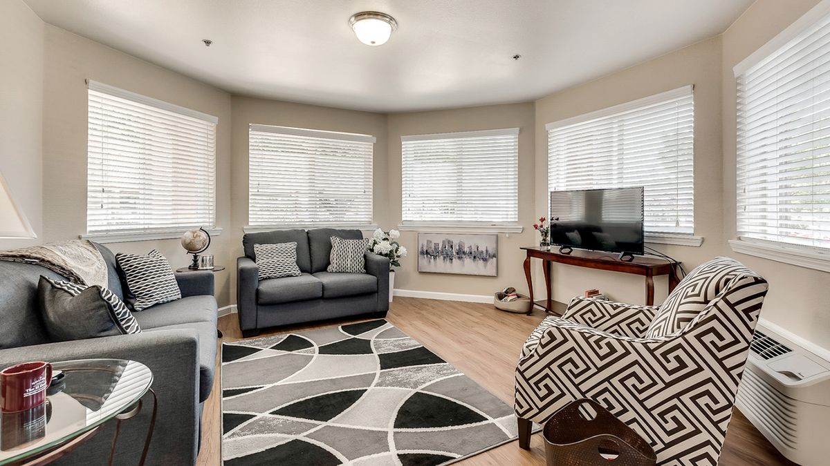 A cozy living room with a sofa, armchair, and a patterned rug on hardwood flooring.
