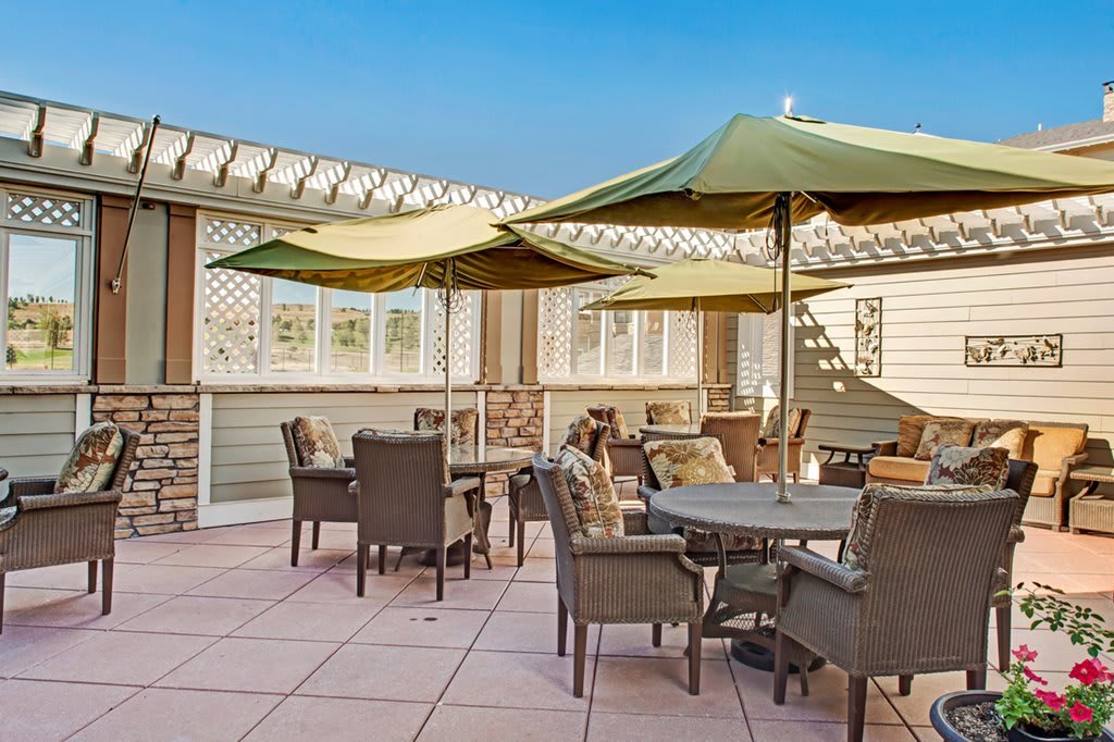 An outdoor patio with tables and chairs shaded by umbrellas, set on a sunny day.