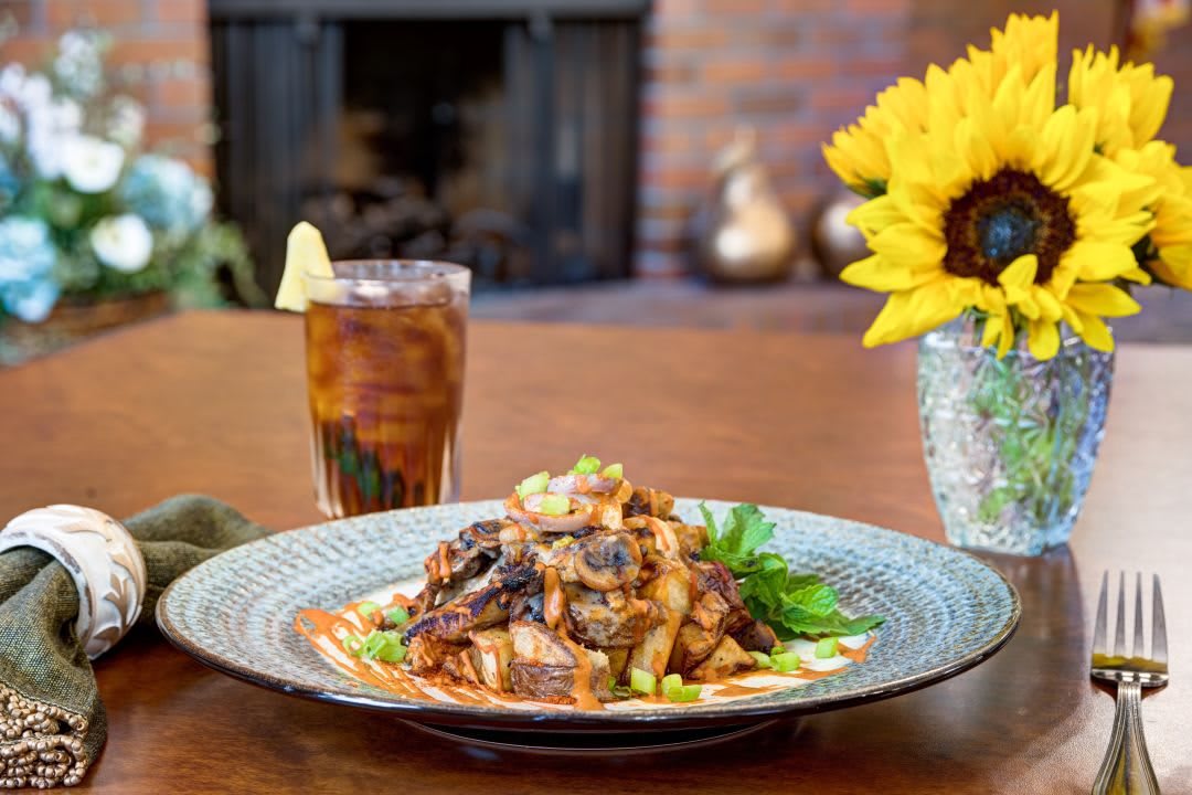 A plated meal with a refreshing drink and sunflower centerpiece on a dining table.
