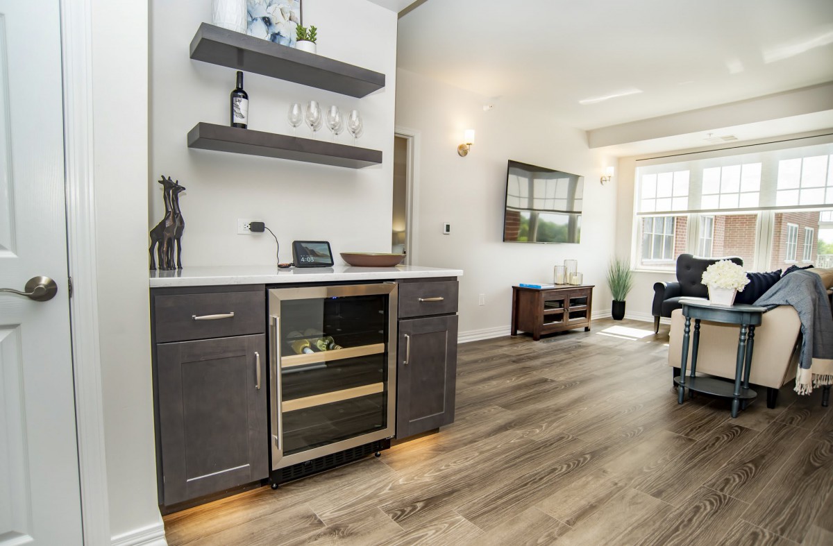 A modern kitchen space featuring a wine fridge and wooden shelves, leading into an open living area.