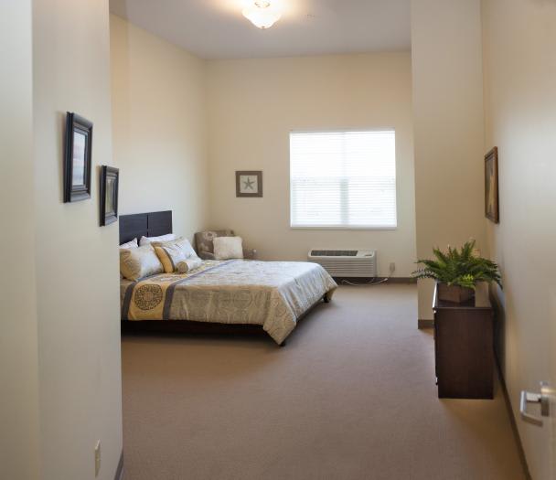 A minimalist bedroom with neutral tones, featuring a neatly made bed, framed pictures, and a potted plant by the window.