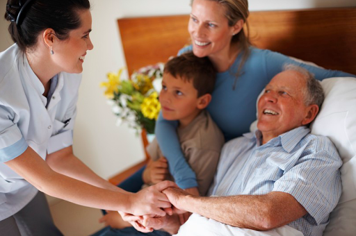 A caregiver interacts warmly with a family, bringing joy to an elderly man and his loved ones.
