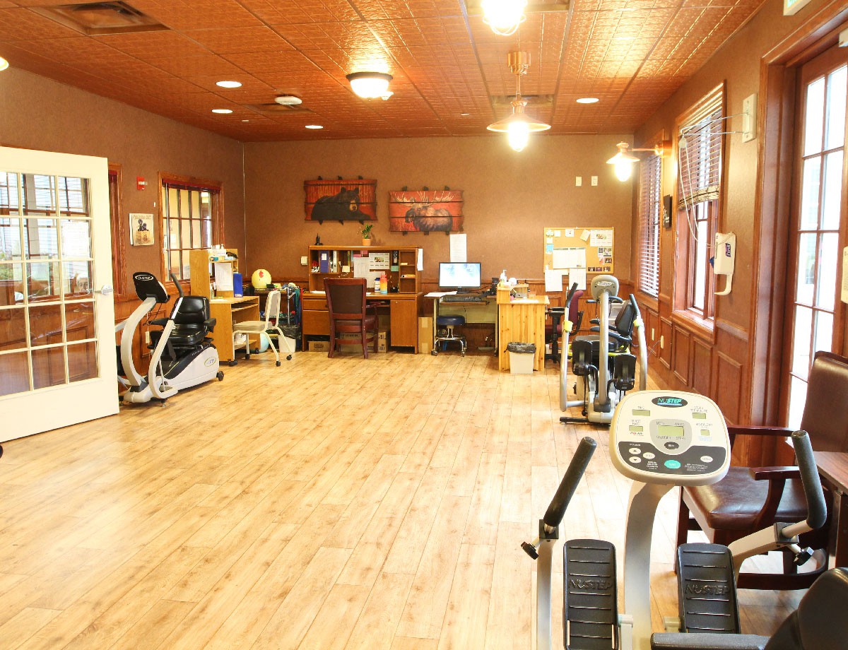 A well-lit gym with exercise machines and a wooden floor.