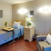 A well-furnished bedroom featuring a single bed, nightstand with a lamp, and an armchair.