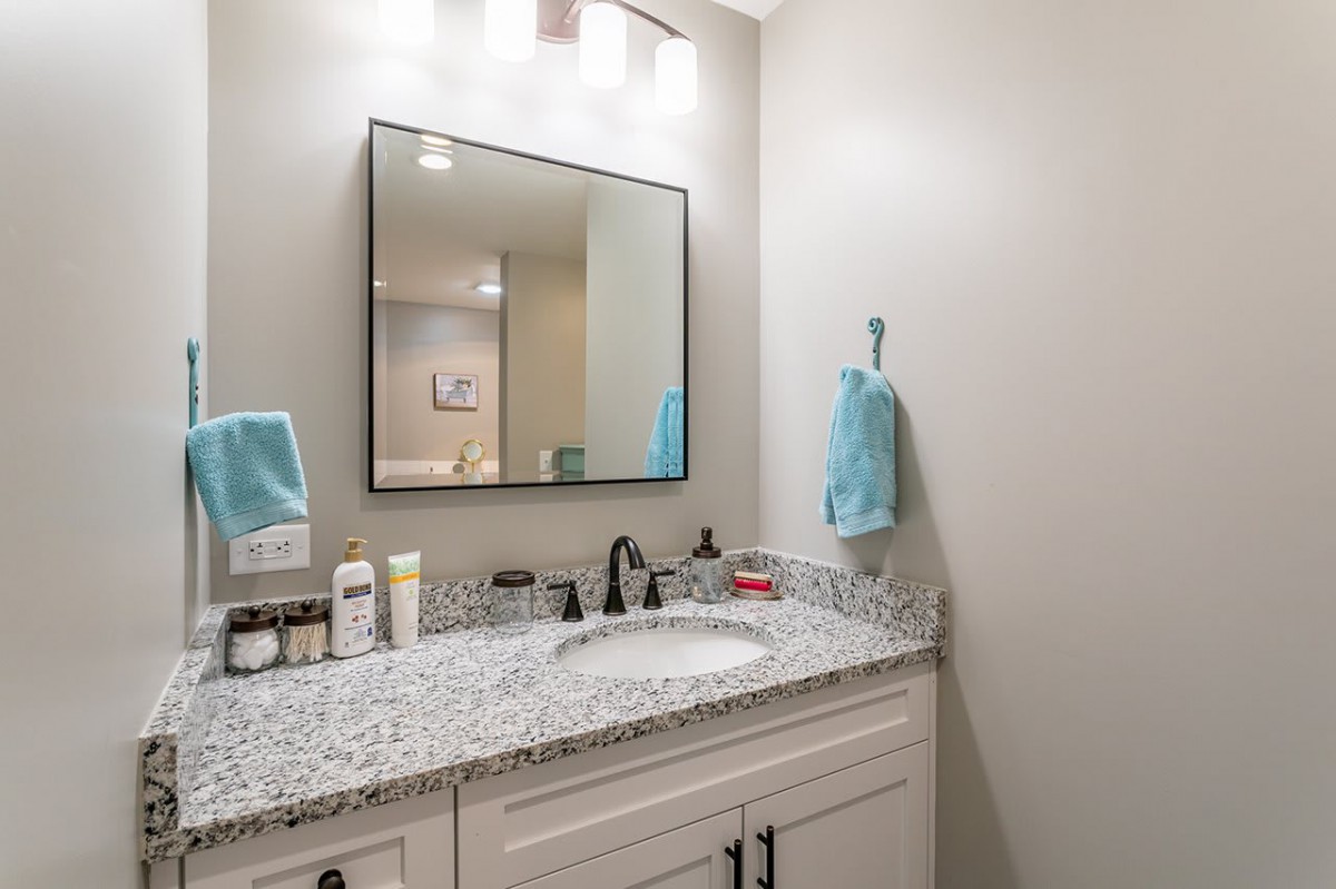 A modern bathroom vanity with a granite countertop and mirror, featuring neatly arranged toiletries and blue towels.