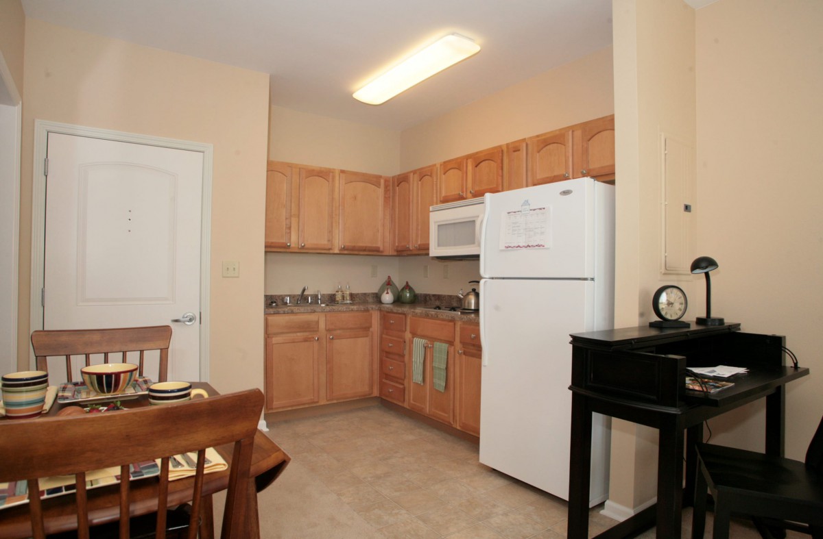 A modern kitchen with wooden cabinets, equipped with a refrigerator and microwave.