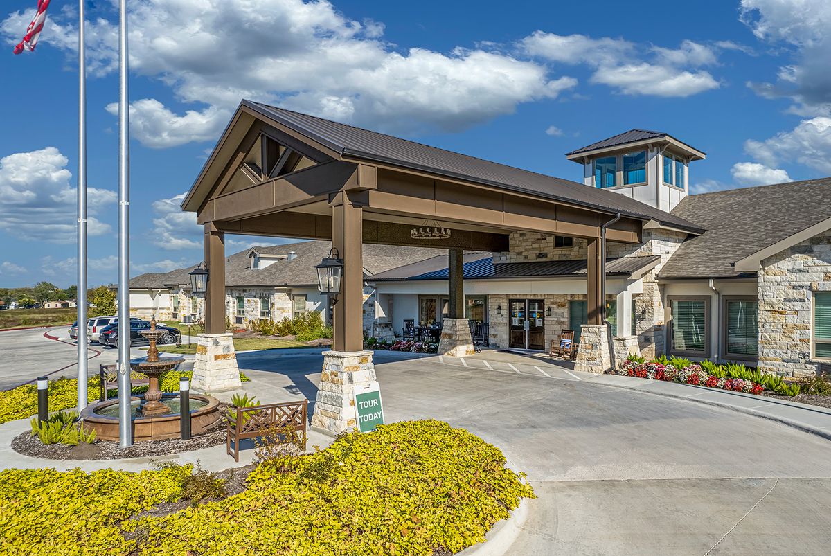 A modern building entrance with a covered driveway and landscaped surroundings under a partly cloudy sky.