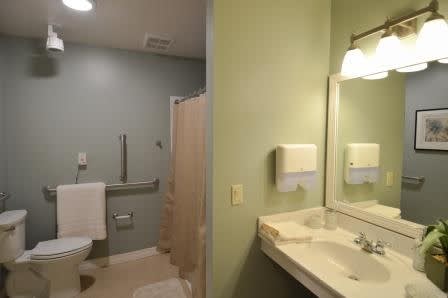A clean, accessible bathroom with a sink, mirror, toilet, and handrails.