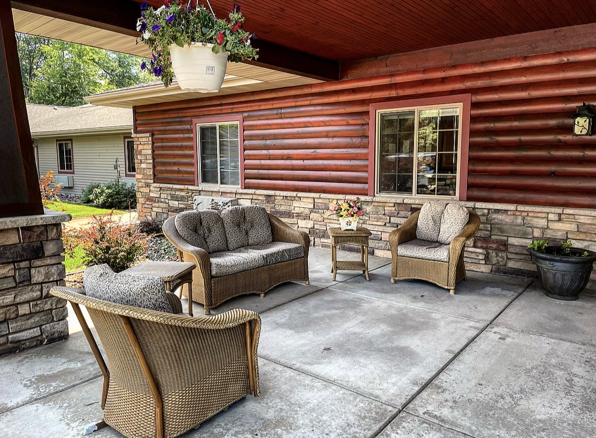 A cozy patio with cushioned outdoor furniture, set against a log cabin and stone wall backdrop.