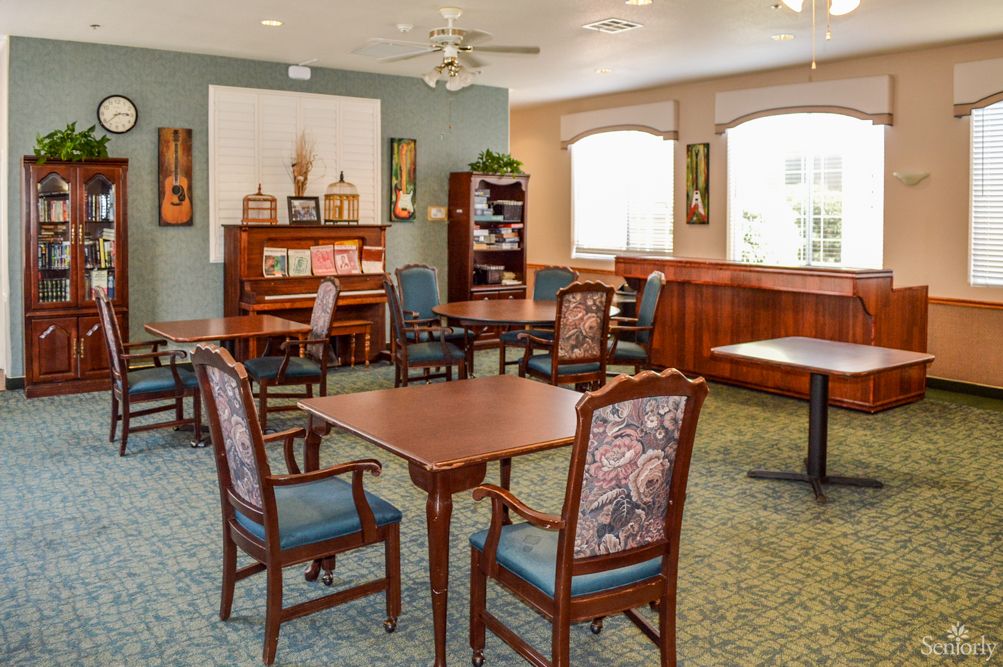 A well-lit room with multiple tables and chairs, featuring a piano and a bookshelf.