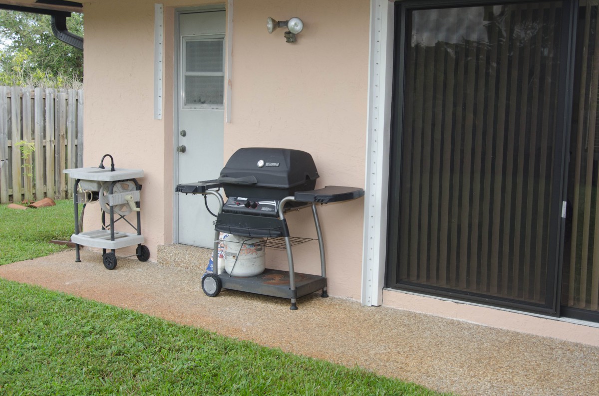 An outdoor patio area with a barbecue grill and propane tank next to a door and window.