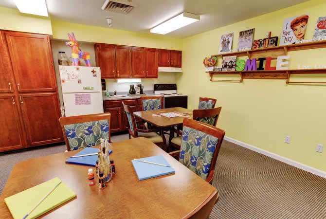 A cozy kitchen and dining area with wooden cabinets, decorated yellow walls, and colorful chairs.