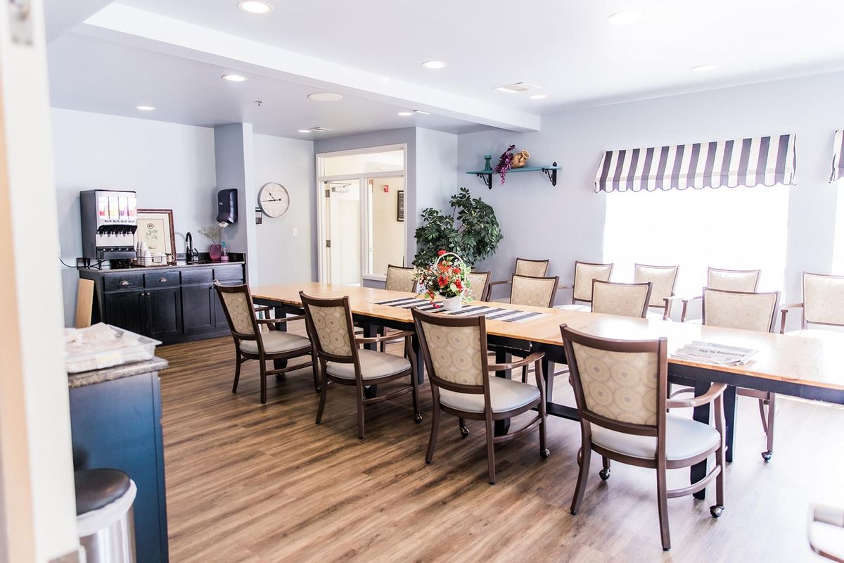 A well-lit dining room with a long table and several chairs, featuring elegant decor and wooden flooring.