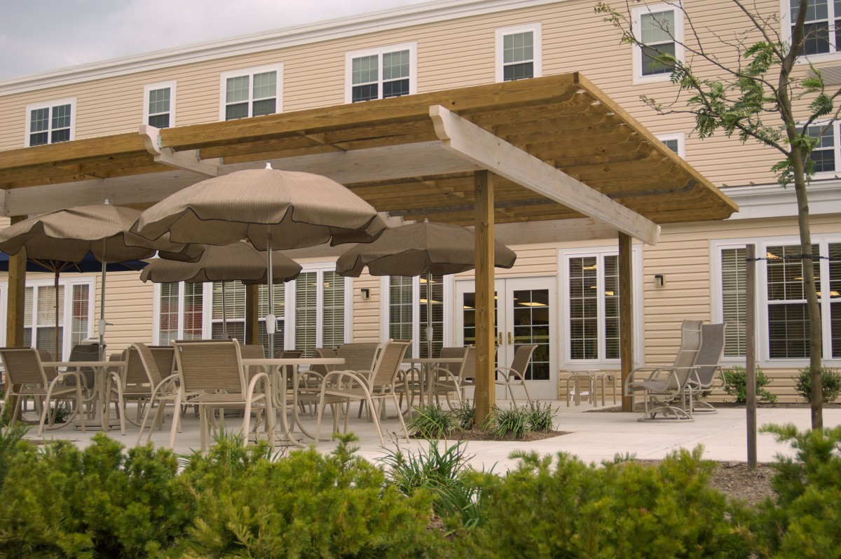 An outdoor patio with tables and chairs under a pergola, featuring large umbrellas for shade.