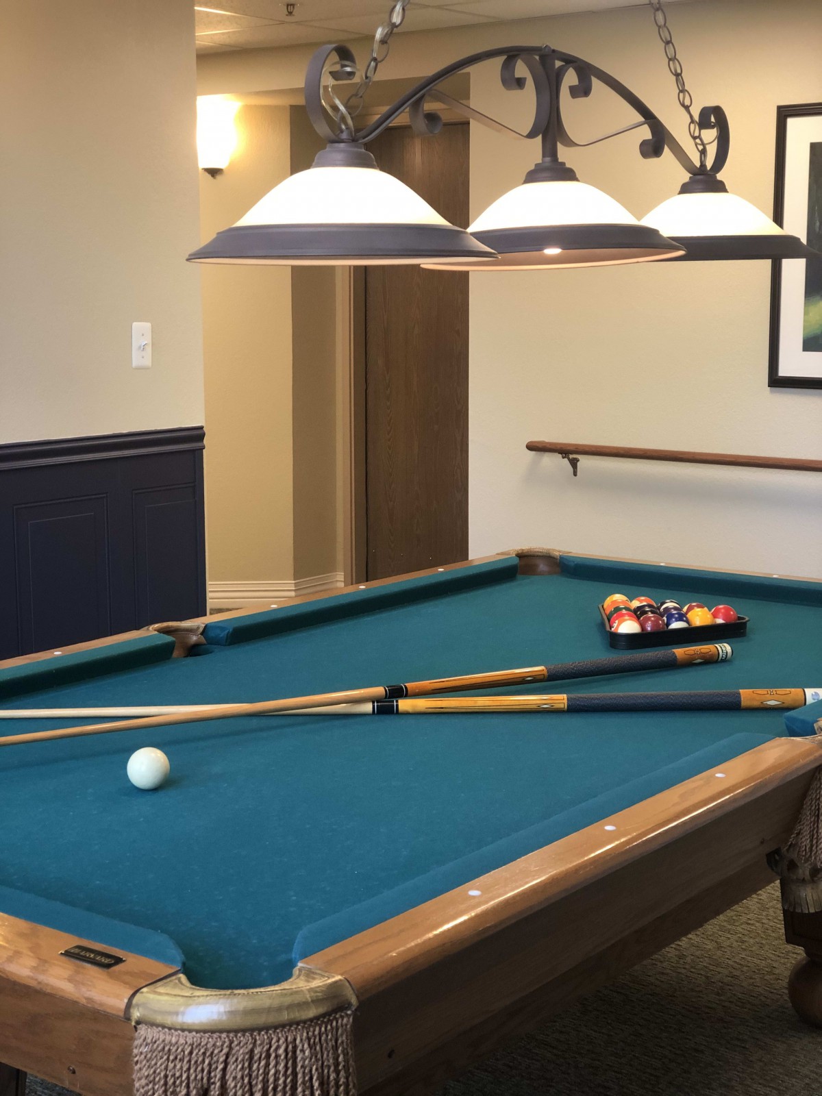 A well-lit game room featuring a billiard table with pool cues and balls ready for play.