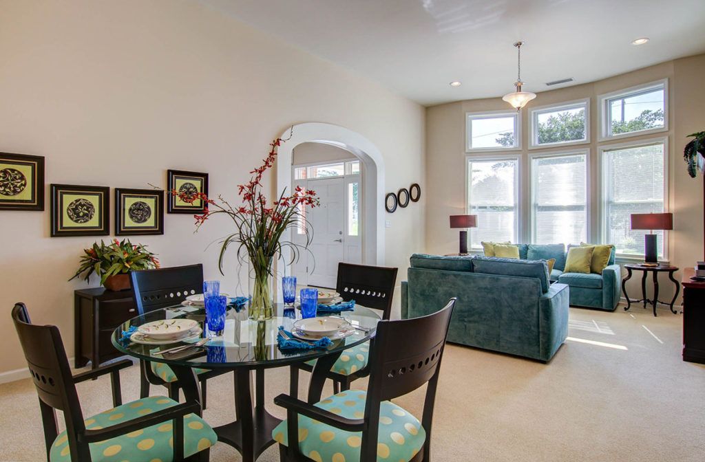 A modern living and dining space with blue accents, featuring a glass dining table set and ample natural light.