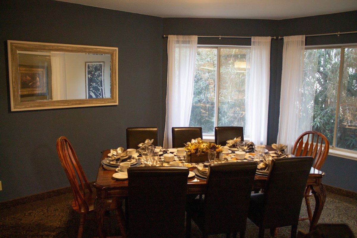 A dining room with a table set for a meal, featuring elegant chairs and a large window with curtains.