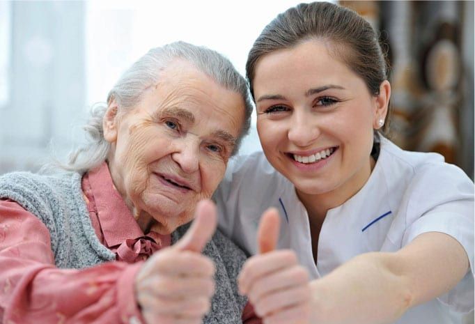 An elderly woman and her caregiver smiling and giving a thumbs up.