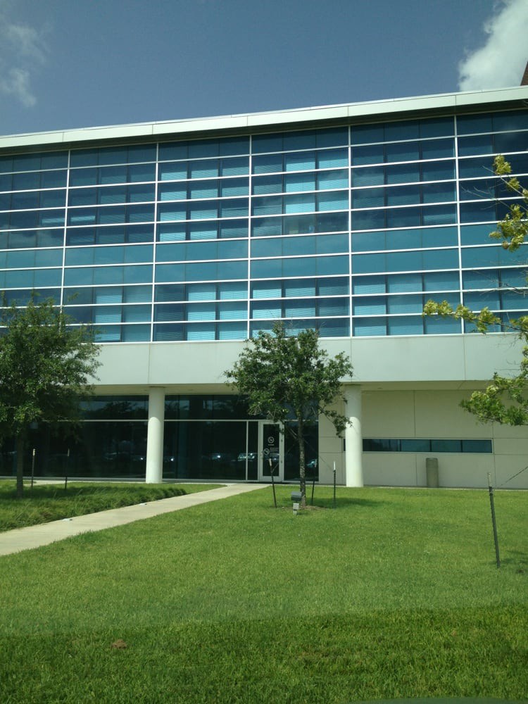 A modern building with a glass facade surrounded by a well-maintained lawn and trees.