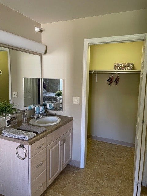 A bathroom featuring a vanity with a sink and a mirror, adjacent to an open closet.