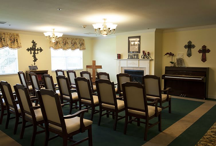 A small chapel interior with rows of chairs facing a cross and a piano.