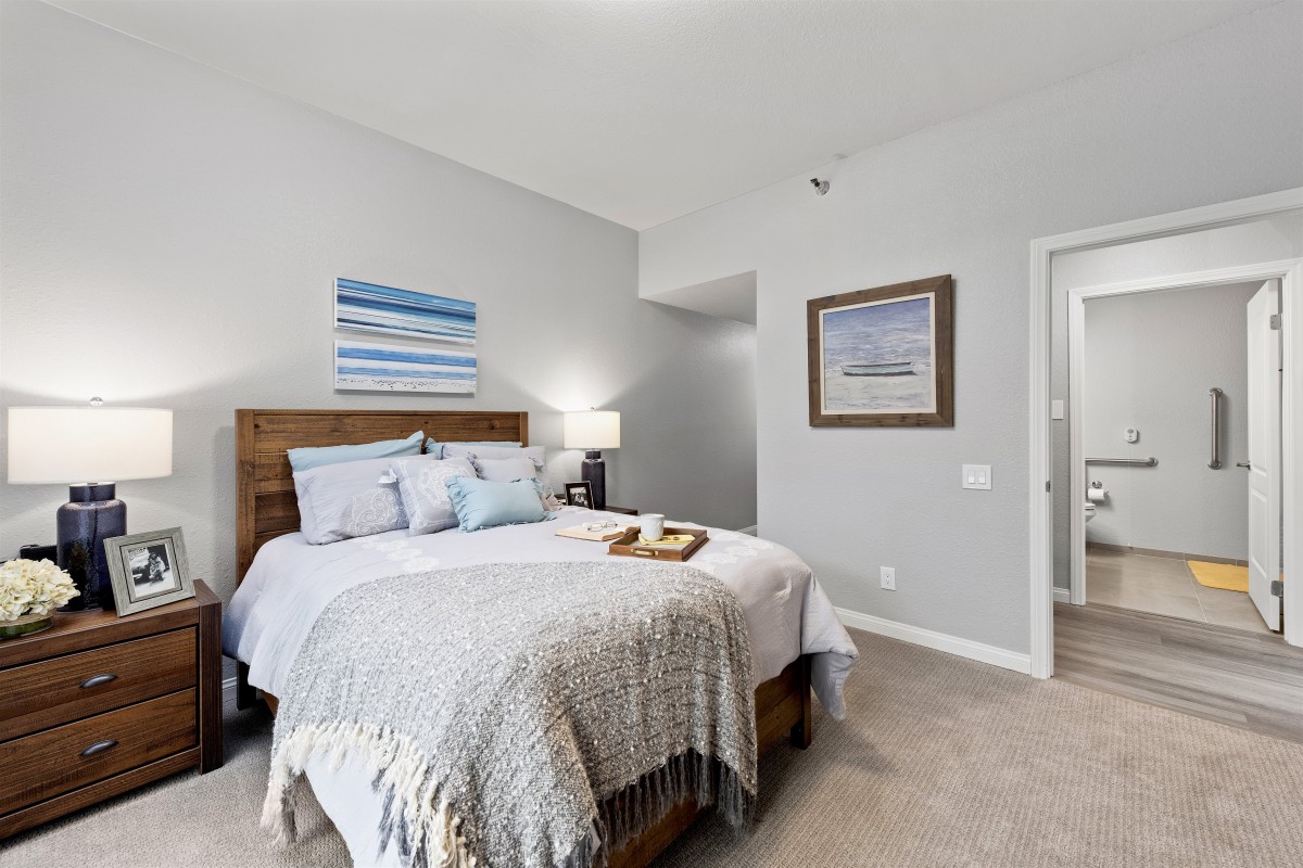 A cozy bedroom with a neatly made bed, wall art, and soft lighting.