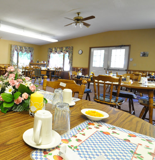 A cozy dining room set up for a meal, featuring wooden tables and chairs with floral decorations.