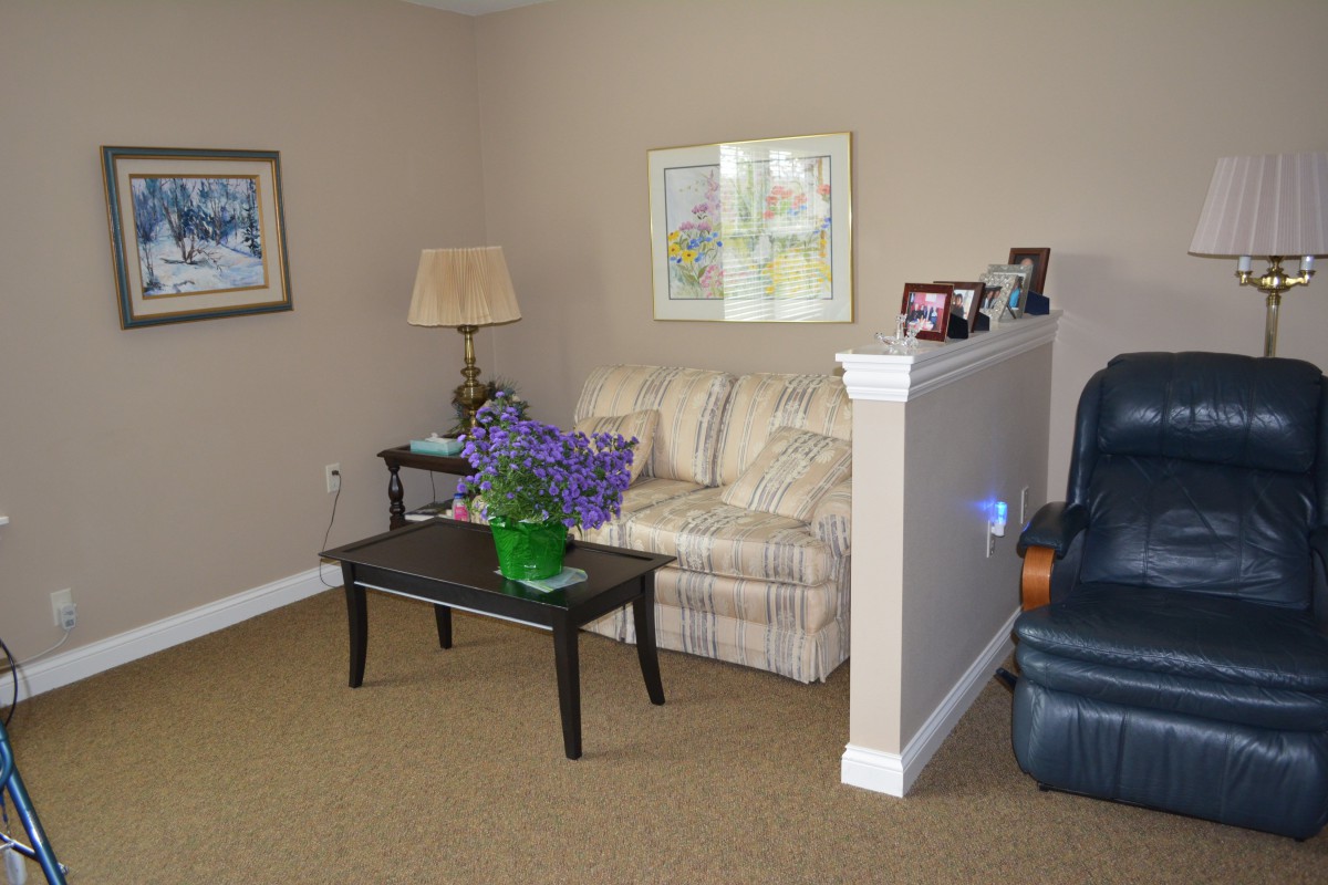 A cozy living room area with a sofa, table, lamp, and framed artwork on the walls.