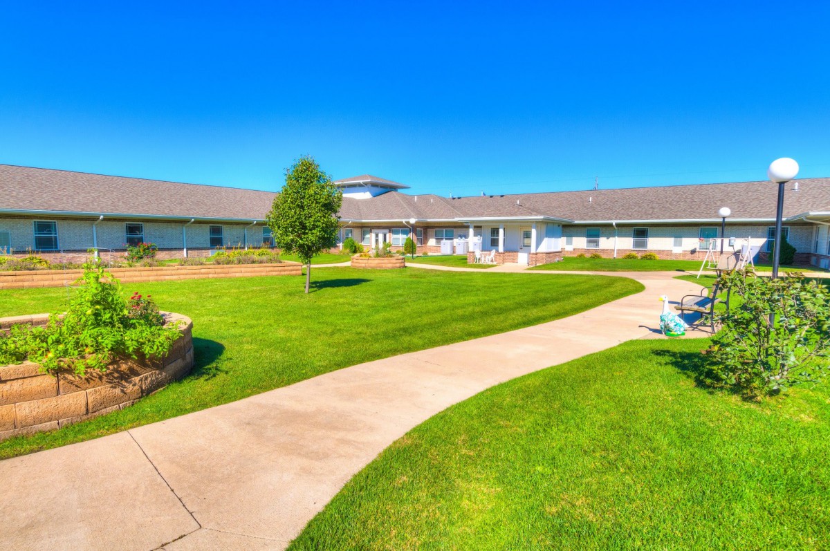 A scenic view of a well-maintained lawn and garden with a winding pathway leading to a building under a clear blue sky.