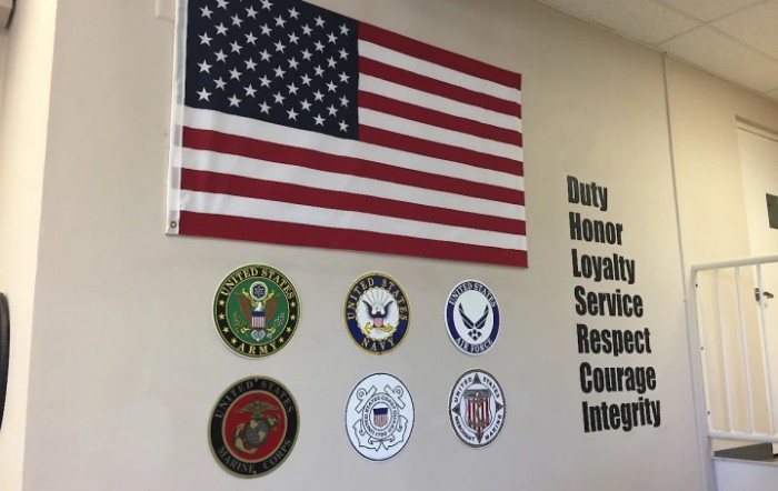 An American flag displayed alongside military insignias and words reflecting core values such as duty, honor, and integrity.