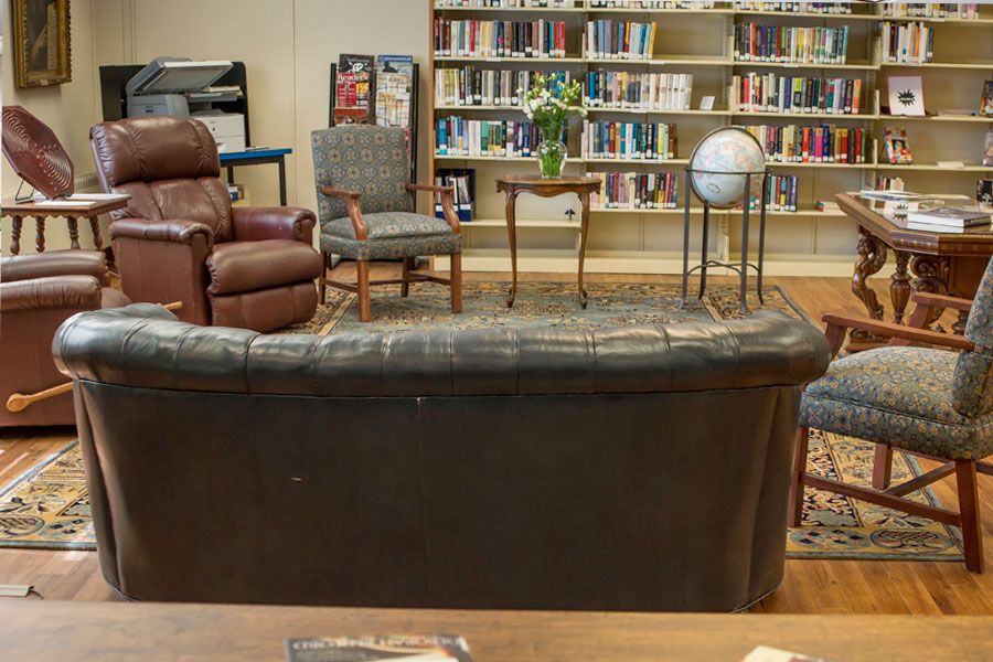 A cozy library setting featuring a sofa, chairs, and a globe in front of a well-stocked bookshelf.